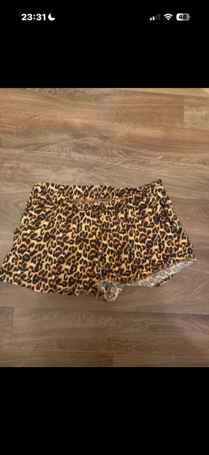 Leopardmönstrade shorts med snörning - Snygga shorts med leopardmönster i bruna och svarta toner. De har snörning framtill med små hjärtformade detaljer och en loose passform. Materialet känns mjukt och lätt, perfekt för varma dagar. Insidan har ett kontrasterande mönster och kanten är lätt vågig.