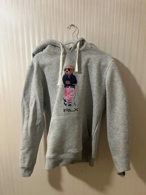 Grå hoodie Polo Ralph Lauren L - Säljer en grå ralph lauren bear hoodie som jag inte vill ha längre och har bara använt den 3 gånger. Den är i storlek L men den passar till S/M. 