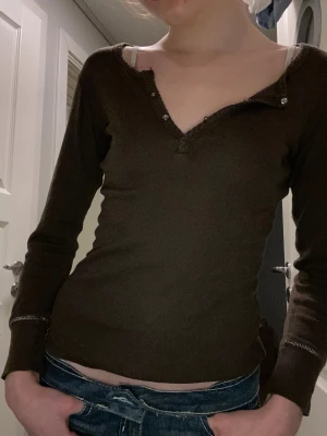 Brun långärmad topp med knappar - Passad brun långärmad med knappar att styla med exempelvis spelstopp under, en knapp är sönder se bild och är för liten för mig