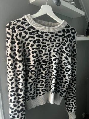 Leopardmönstrad stickad tröja - Säljer en stickad tröja med leopardmönster i svart och vit. Tröjan har rund halsringning och ribbade muddar vid ärmslut och nederkant. Perfekt för dig som gillar djurmönster och vill ha en mysig och trendig look.