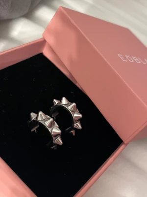 Silvriga spike-örhängen från Edblad - Coola örhängen från Edblad i silverfärgad metall med tydliga spikes runt hela ringen. De har en chunky design som ger en edgy vibe och kommer i original ask. Perfekta för dig som vill sticka ut med din stil. 