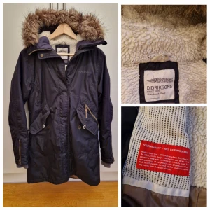 Svart parkas från Didriksons - Svart parkas från Didriksons med teddyfoder huva med avtagbar fuskpäls. Jackan har dragkedja, knappar, flera fickor och är vind- och vattentät. Finns två små fläckar (som kanske går att ta bort). Teddy fodret i nacken är lite mörk färgat. I övrigt en fin jacka som har mycket kvar att ge! 