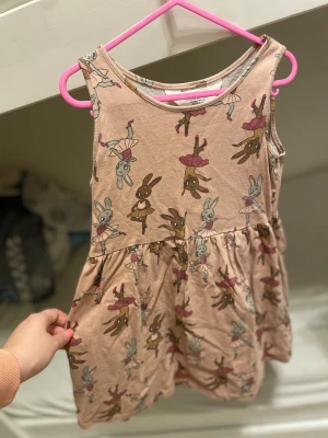 Beige klänning med kaniner H&M 122/128 - Supersöt beige armlös klänning från H&M i storlek 122/128. Klänningen har ett gulligt mönster med dansande kaniner i rosa kjolar och ballerinaskor. Mjuk och skön bomull, perfekt för vår och sommar. Rund halsringning och utställd kjol för extra snurr. Barn till tjejer 