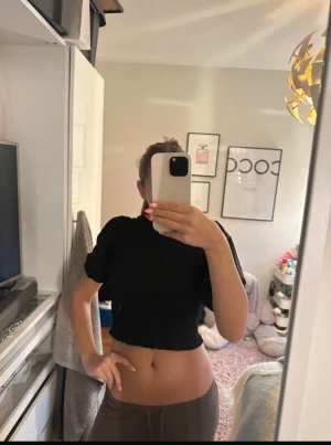 Svart smockad topp med puffärm - En svart croppad topp med smockat tyg och korta puffärmar. Hög halsringning och elastisk passform som sitter tajt mot kroppen. Perfekt för att lyfta en enkel outfit med en trendig touch.