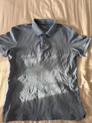 Ljusblå pikétröja från Dressmann - Snygg ljusblå pikétröja från Dressmann i storlek M. Tröjan har klassisk krage, två knappar framtill och är kortärmad. Använd fåtal gånger