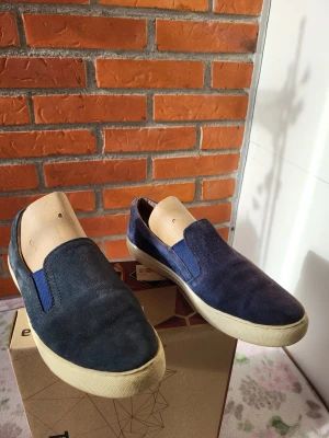 DASIA Slip-ons, navy Blå, Storlek 38 - Ett par bekväma slip-ons från Dasia. Perfekt för en avslappnad men stilren look. Skorna är i bra skick och redo för nya äventyr. Obs. Olika navy nivåer pga solen kolla bilder
