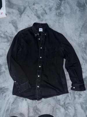 Svart overshirt från Zara i bomull - Funkar för både M o S. Skjortan har en bröstficka och vita knappar som kontrast. Tillverkad i mjuk bomull, långärmad och med en stilren, enkel design som funkar till många olika looks.