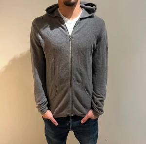 Grå cardigan/tröja från Ljung Marcus Larsson - Säljer en stilren grå hoodie från Ljung Marcus Larsson i storlek M. Tröjan har dragkedja framtill, huva och två fickor. Materialet är mjukt och stickat, perfekt för chill dagar. Passformen är normal och ärmarna är långa. NYPRIS:1699Kr Mitt pris:379Kr