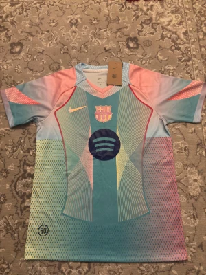 Barcelona 25/26 specialutgåva - Säljer en Barcelona x Nike fotbollströja med Spotify-logga, i en unik mix av ljusblå, rosa och mintgrön. Tröjan har korta ärmar, V-ringad krage och coola grafiska linjer och prickar. Materialet är lätt och andas, perfekt för match eller träning. FCB-emblem på bröstet.