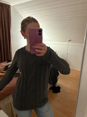 Grå stickad tröja Colours of the World - Mysig grå stickad tröja från Colours of the World i storlek XS. Tröjan har ett snyggt flätmönster framtill, rund halsringning och långa ärmar. Perfekt för kyliga dagar och enkel att matcha med jeans eller kjol.