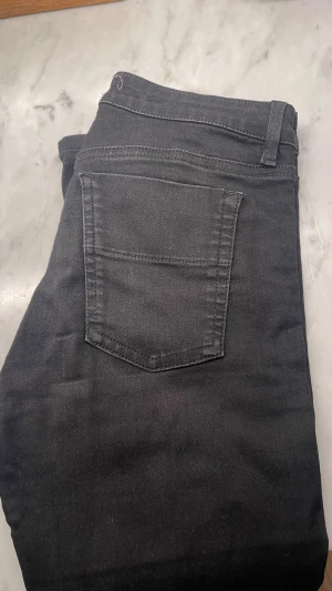 Filippa K Svarta jeansbyxor i slim fit - Filippa K Snygga svarta jeansbyxor med klassisk femficksdesign och smal passform. Byxorna har bälteshällor och är tillverkade i ett stretchigt jeanstyg som sitter skönt hela dagen. Perfekta för dig som gillar en stilren och enkel look.