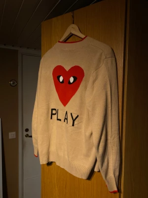 Unik kofta från Comme des Garçons Play - Säljer en unik kofta från Comme des Garçons Play med ikoniskt rött hjärta med ögon på både fram- och baksidan. Koftan har knappar framtill, ribbade muddar och röda detaljer vid hals och ärmslut. Perfekt för dig som gillar coola prints och vill sticka ut.