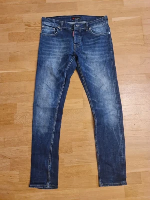 Replay Anbass blå jeans slim fit - Snygga Dsquared2 jeans i klassisk blå tvätt med slitningar och smal passform. Modellen har fem fickor, dragkedja och knappstängning. Perfekt för dig som gillar en modern och stilren look. Materialet är mjukt jeans-tyg som sitter skönt hela dagen.