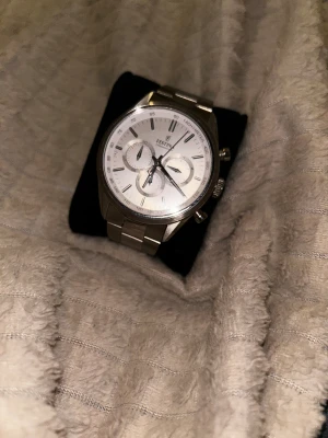 Silverfärgad Festina Chronograph klocka - Stilren Festina Chronograph herrklocka i silver med metallarmband och vit urtavla. Klockan har tre mindre subdials, tachymeter runt urtavlan och tydliga indexmarkeringar. Länken är robust och har Festina-logga på spännet. Perfekt för dig som gillar klassisk design.