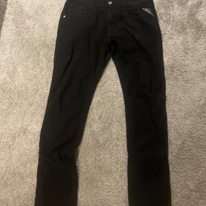 Svarta Replay Anbass jeans, stl 32 - Svarta jeans från Replay, modell Anbass. Klassisk femficksdesign med Replay-logga på fickan. Snygg, smal passform och stilren look som funkar till det mesta. Tillverkade i mjukt och stretchigt jeanstyg för extra komfort.