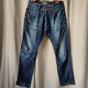 Mörkblå jeans från Grant - Snygga mörkblå jeans från Grant med klassisk femficksdesign och kontrastsömmar. Jeansen har en rak passform och är perfekta för en avslappnad stil. De har en knappgylf och bälteshällor för extra komfort.