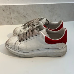 Alexander McQueen -  vita sneakers från Alexander McQueen med röd mockadetalj på hälen och bred sula. Används inte längre, kom privat vid frågor eller bud 