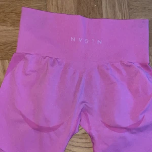 Rosa seamless leggings från NVGTN - Säljer ett par rosa seamless leggings från NVGTN med hög midja och tight passform. De är tillverkade i ett stretchigt syntetmaterial och har diskreta konturdetaljer längs benen och rumpan. Perfekta för träning eller chill.