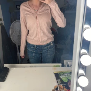 Ljusrosa kofta från The Shirt Factory - Supersöt ljusrosa kofta från The Shirt Factory, designad av Linnéa Braun. Koftan har v-ringning, pärlknappar och ribbade muddar. Perfekt att slänga över en topp för en chill look. Långärmad och i mjukt material som känns skönt mot huden.