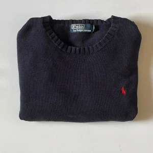 Mörkblå stickad tröja Polo Ralph Lauren - Säljer en klassisk mörkblå stickad tröja från Polo Ralph Lauren i storlek M. Tröjan har rund halsringning, långa ärmar och den ikoniska röda broderade loggan på bröstet. Perfekt att styla med jeans eller chinos för en clean look. .