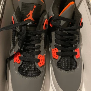  Air Jordan 4 Retro grå/svart/röd - Nike Air Jordan 4 Retro sneakers i grått och svart med röda detaljer. Skorna har klassisk meshpanel, svarta skosnören och vit sula med synlig Air-enhet. Som är i storlek 41 och kostar 1300kr