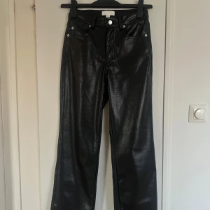 Svarta croc-mönstrade skinnbyxor  - Säljer ett par svarta byxor från H&M i storlek 34 med croc-mönstrad yta. Byxorna har raka ben, normal passform och är gjorda i ett syntetmaterial som ser ut som skinn. Klassisk femficksmodell med bälteshällor och dragkedja.