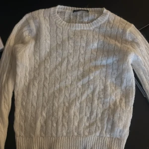 Vit kabelstickad tröja Brandy melville  - Mysig vit kabelstickad tröja från brandy med rund halsringning och långa ärmar. Perfekt för kyliga dagar och enkel att matcha med jeans eller kjol. Tröjan har ribbade muddar och klassisk kabelstickad struktur.