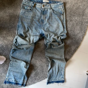 Ljusblå jeans från 2Y Studios - Säljer ett par ljusblå jeans från 2Y Studios med klassisk femficksdesign och råa, fransiga benslut. Jeansen har normal passform och raka ben. Tillverkade i jeansmaterial med snygg tvättad look och detaljerade sömmar.