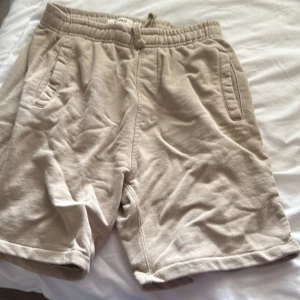 Beige mjuka shorts med snörning - Säljer ett par sköna beige shorts från L.BREAD med elastisk midja och snörning. De har två sidofickor och är gjorda i mjukt bomullsmaterial, perfekta för chill dagar. Passformen är normal och färgen är ljusbeige.