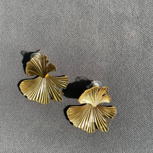 Guldiga örhängen i bladform WOS - Säljer ett par statement örhängen i guldmetall med snygg bladform från det lyxiga märket WOS. De har en cool, organisk design som verkligen sticker ut och passar perfekt när du vill addera lite extra till din look.