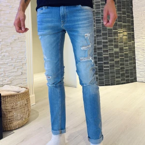Ljusblå slitna jeans Jack & Jones 29/32 - Ljusblå jeans från Jack & Jones med snygga slitningar och trasiga detaljer på benen. Modellen är slim och har klassisk femficksdesign. Jeansen är tillverkade i bomull och har en fräsch, modern look med uppvikta benslut.