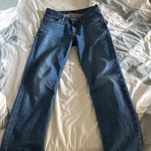 Blå raka jeans från Lee - Klassiska blå jeans från Lee med raka ben och normal passform. Jeansen har fem fickor, Lee-logga på bakfickan och läderpatch i midjan. Tillverkade i slitstarkt denim med snygga kontrastsömmar. Perfekta för en avslappnad och tidlös look. W29 L32