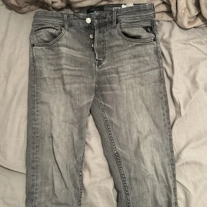 Replay Grover grå jeans straight fit - Snygga Replay Grover jeans i en tvättad grå färg med straight fit. Klassisk femficksmodell, svarta detaljer på bakfickorna och tydlig Replay-label bak. Jeansen har knappgylf och är tillverkade i jeansmaterial med en cool, lite sliten look. Storlek W29 L32
