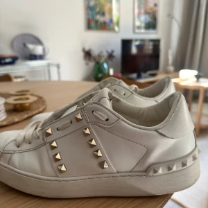 Valentino Rockstud vita sneakers - Vita Valentino Rockstud sneakers i skinn med guldfärgade nitar längs sidorna. Köpta 2023 för 7500 kr, dem är väl använda så det finns lite slitningar. 