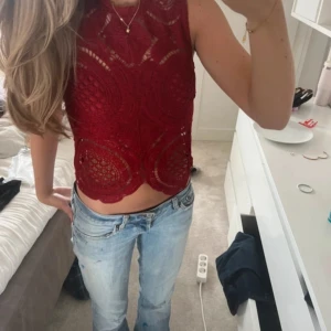 Vinröd spetsig linnetopp - Säljer en vinröd croppad linnetopp med snyggt spetsmönster och rund halsringning. Toppen är ärmlös och har en unik, vågig nederkant. 