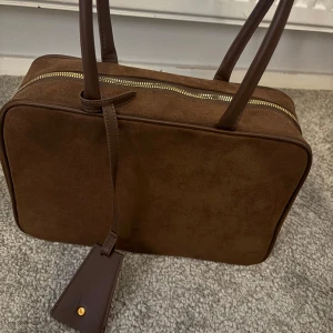 Brun axelväska   -  Brun axelväska i mocka. Perfekt för dig som gillar klassisk och enkel design. Köpt från second hand 