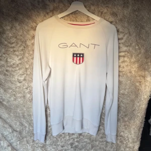 Vit långärmad tröja från GANT - Vit långärmad tröja från GANT med broderad logga och sköld på bröstet.