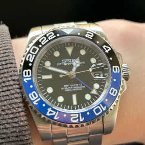 Seiko mod GMT ”Batman” 40mm - Hej! Detta är en Seiko mod. Gmt funktion så det går att hålla koll på flera tidzoner samtidigt. Automatiskt Nh34 movement och grön lume som lyser i mörkret. Klockans diameter är 40mm. Medföljer extralänkar. Finns repor på armbandet men inget som syns jätte tydligt, dm vid frågor!
