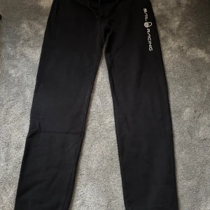 Svarta mjukisbyxor från Sail Racing - Svarta mjukisbyxor från Sail Racing med logga tryckt längs ena benet. Byxorna har resår och snörning i midjan samt muddar vid bensluten. Tillverkade i mjukt material som är perfekt för chill eller träning. Skicket är 9,5/10, använda fåtal gånger! 