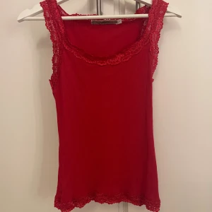 Röd ribbad linnetopp med spets - Säljer en snygg röd linnetopp från Aéryne med ribbad struktur och spetsdetaljer vid halsringning, axlar och nederkant. Toppen är ärmlös och har en feminin, figurnära passform som ger en chic vibe. Perfekt att styla med jeans eller kjol för en cool look. I stork L men omsydd till storlek S eller XS