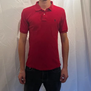  pikétröja från Polo Ralph Lauren - Röd pikétröja från  Ralph Lauren med klassisk krage och två knappar framtill. Tröjan har korta ärmar och den ikoniska broderade loggan på bröstet. Tillverkad i bomull för en skön och luftig känsla. Perfekt för en clean och stilren look. Storlek är L o barn och motsvarar ungefär XS-S skulle jag säga Modellen är 180cm.