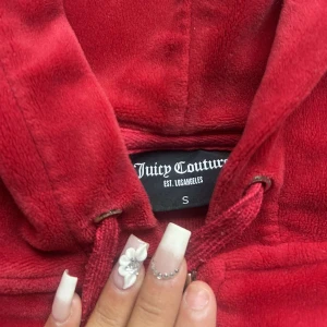 Röd velour hoodie Juicy Couture - Juicy Couture hoodie & byxor i röd, byxor xs tröja S användes förra året någons gånger dragkedjan på tröjan är halvt av å snörena på byxorna metallen är oxå av där man annars i bra skick, pris kan diskuteras 