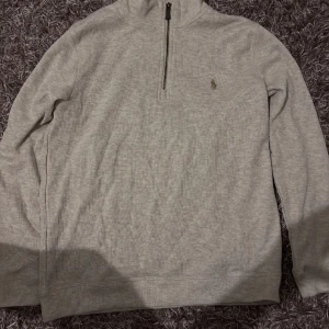 Beige half zip tröja från Ralph Lauren - Snygg ljusgrå långärmad tröja från Ralph Lauren med half zip och klassisk broderad logga på bröstet. Perfekt för lager-på-lager och chill stil. Mjuk bomullskänsla och normal passform.