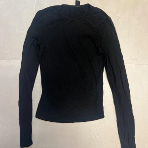 Svart långärmad tröja  - En enkel svart långärmad tröja i mjuk material . Modellen är tight och har rund halsringning, perfekt att ha som basplagg . Stilren och lätt att matcha med allt i garderoben.