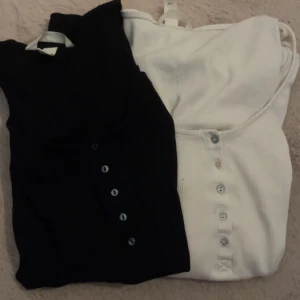 Svart och vit ribbad långärmad topp XS - Två långärmade ribbade toppar i svart och vitt med rund halsringning och knappar framtill. Snygg slim passform och stretchigt material som sitter tajt mot kroppen. 