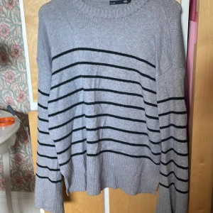 Grå randig stickad tröja 157 S - Grå stickad tröja från 157 i storlek S med svarta horisontella ränder. Tröjan har rund halsringning, ribbade muddar och en loose fit. Perfekt för lager-på-lager och chill dagar. Materialet är mjukt och skönt, passar dig som gillar enkel men snygg stil.