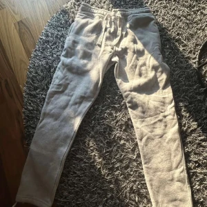 Ljusgrå mjukisbyxor med snörning - Ljusgrå mjukisbyxor från Russermerch med vita snören i midjan och resår. Byxorna har normal passform, sidofickor och är tillverkade i mjukt bomullsmaterial. 