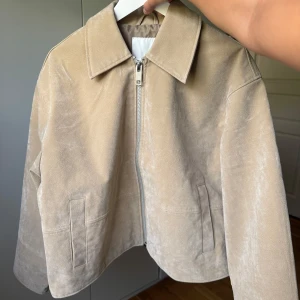 Beige mockajacka med dragkedja - Stilren beige mockajacka från NA-KD med rak passform och silverfärgad dragkedja framtill. Säljer då den var lite för stor på mig! Nypris 1199🫶🏼 säljer för 1100