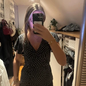 Svart omlottblus med vita prickar Stockh LM - Säljer en svart omlottblus från Stockh LM i storlek XS. Blusen har vita prickar, korta volangärmar och knyt i midjan. V-ringad och med feminin passform, perfekt för dig som gillar trendiga detaljer och mönster.