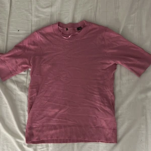 Rosa stickad tröja XS - Snygg rosa stickad tröja i storlek XS med rund hals och ribbade muddar vid ärmslut och nederkant. Tröjan har korta ärmar och är perfekt för dig som gillar en enkel men färgstark look. Passar dig som vill ha något bekvämt och stilrent.